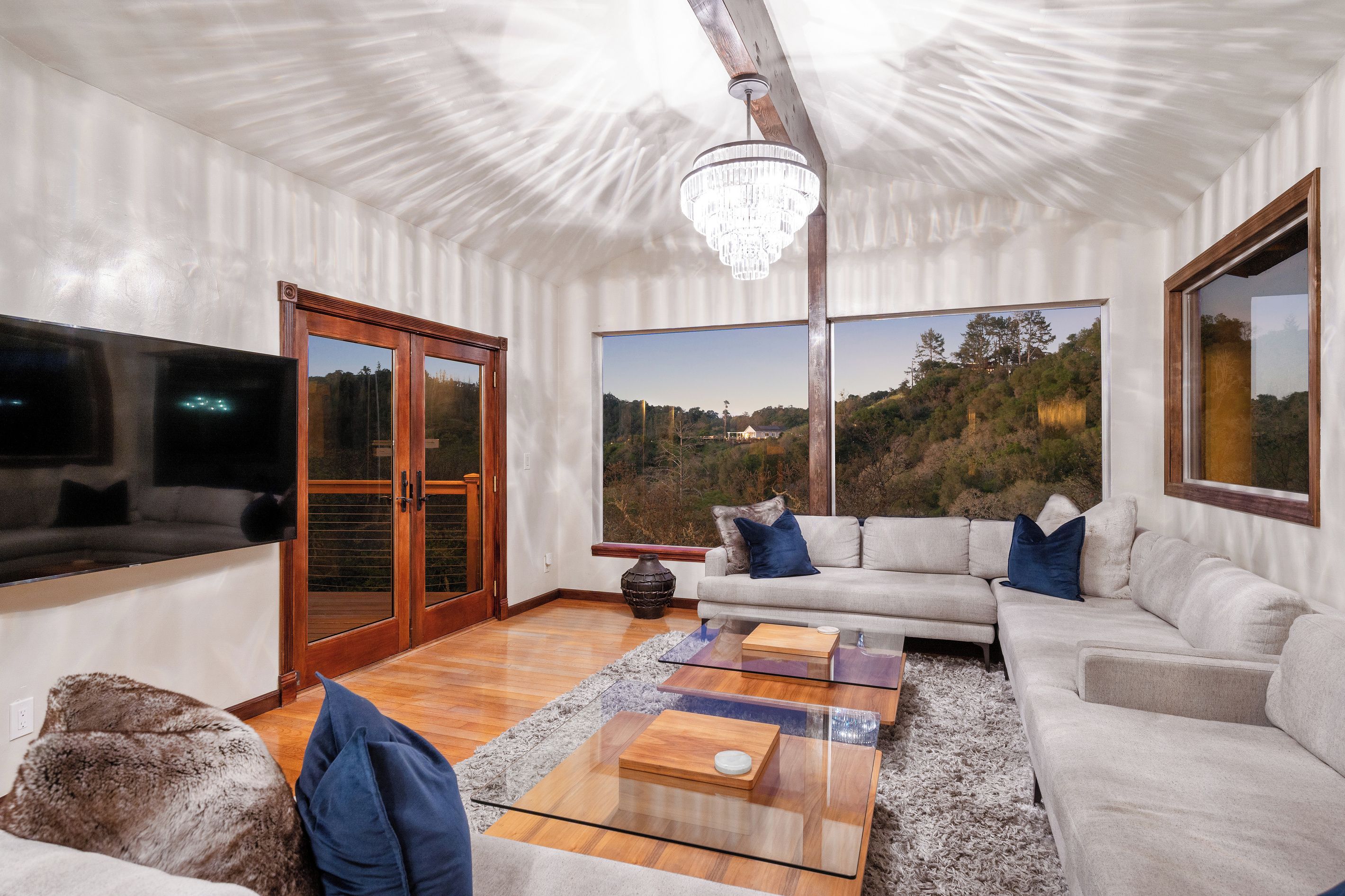 A modern living room with a large window, a chandelier, and a sectional sofa.