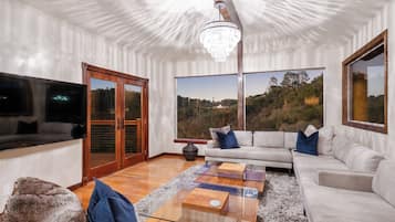 A modern living room with a large window, a chandelier, and a sectional sofa.