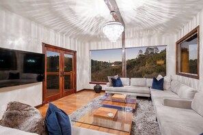 A modern living room with a large window, a chandelier, and a sectional sofa. - Farpoint: Heated Infinity Pool, Mountain Views (Santa Rosa)