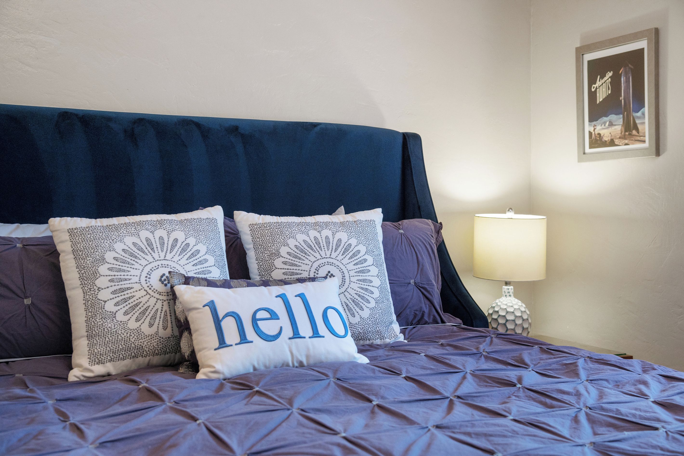 A bed with a blue headboard, multiple pillows with intricate patterns, and a 'hello' pillow.