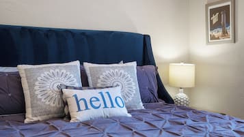 A bed with a blue headboard, multiple pillows with intricate patterns, and a 'hello' pillow.