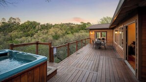 Une terrasse en bois avec un jacuzzi, des sièges d’extérieur et une vue sur une colline boisée.