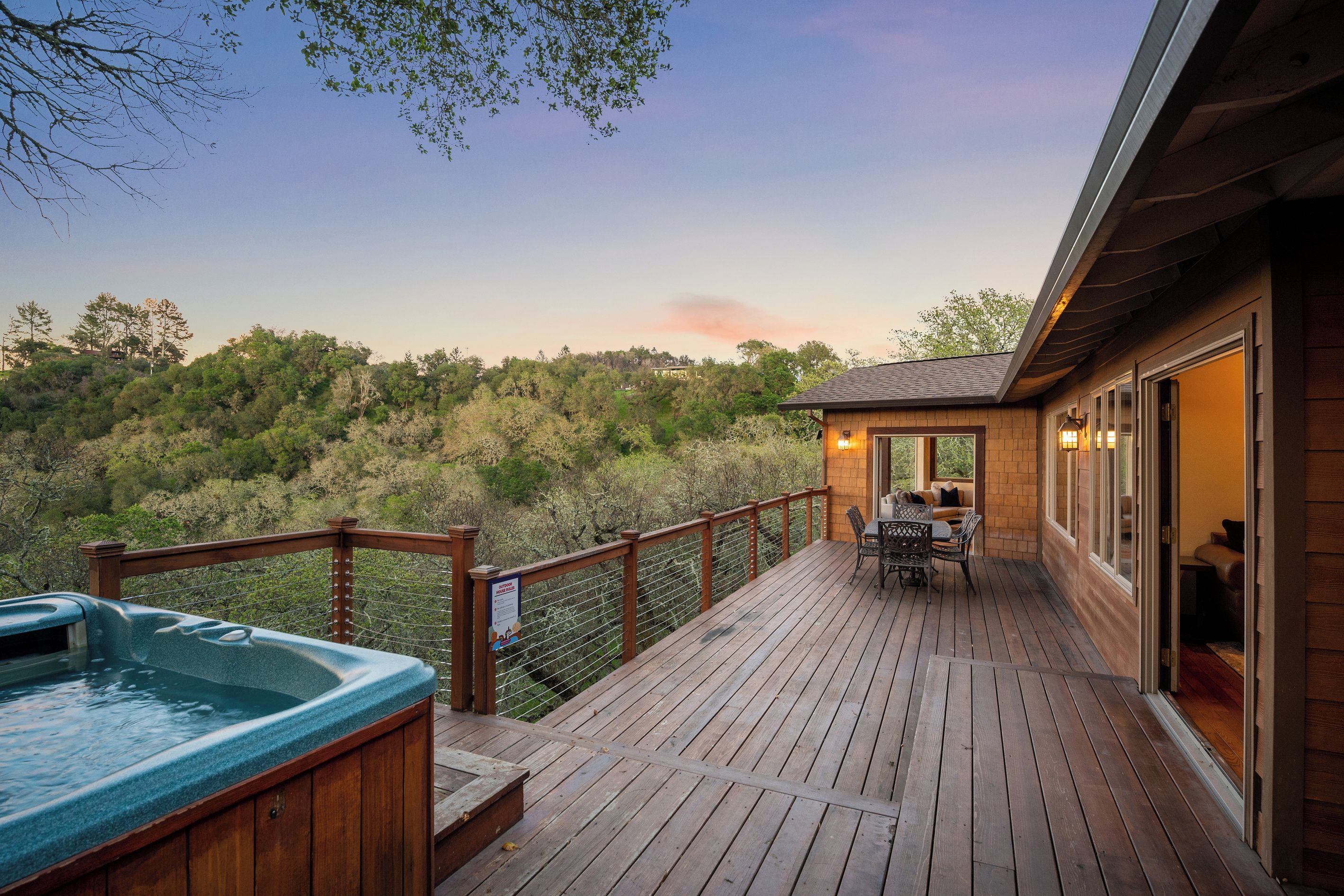 A wooden deck with a hot tub, outdoor seating, and a view of a forested hillside.