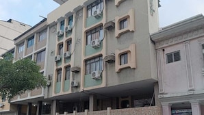 Um edifício de vários andares com telhado plano, aparelhos de ar condicionado e entrada com portão.