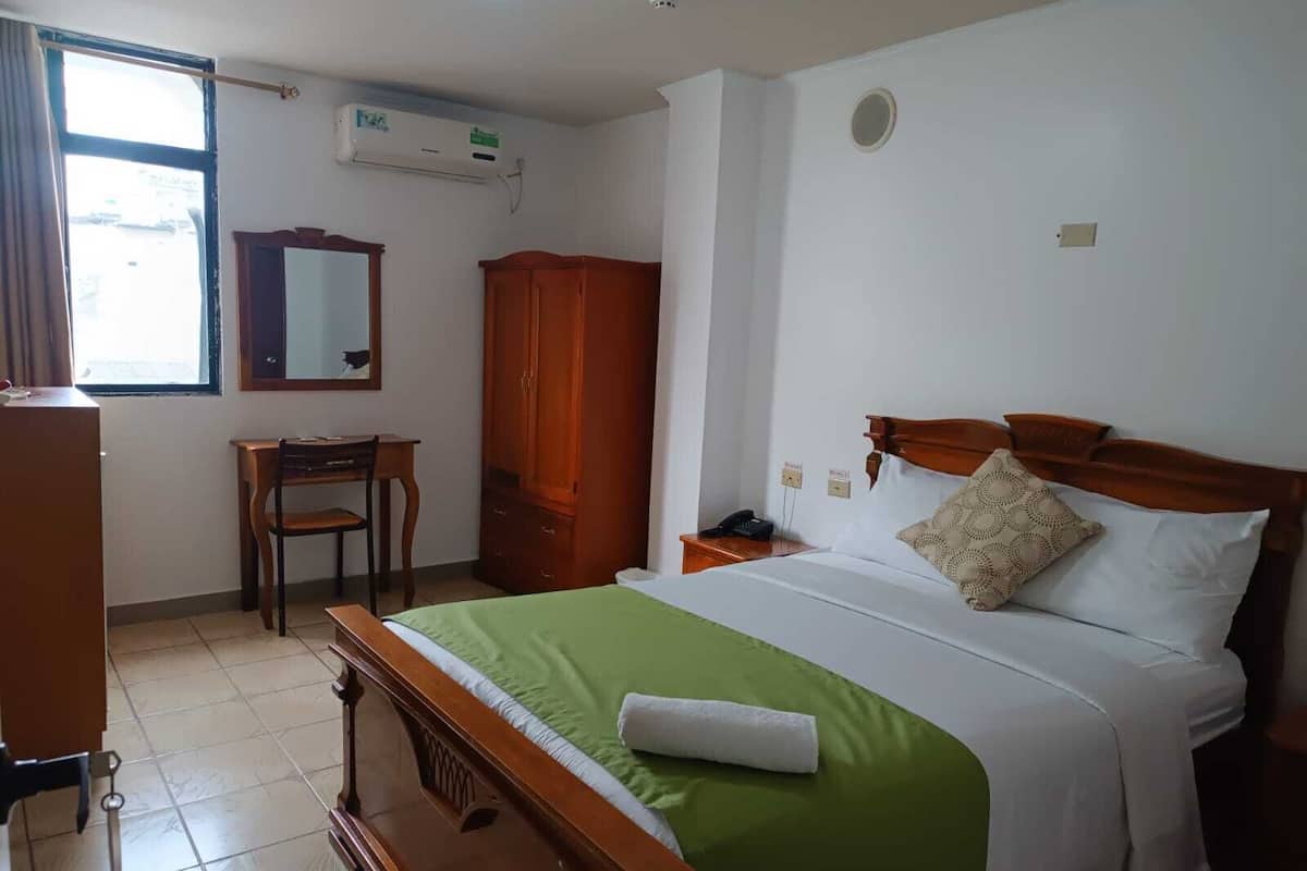 A hotel room with a bed, a desk, a chair, a wardrobe, and a mirror.