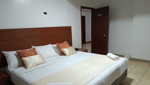 Uma cama bem arrumada com cabeceira de madeira, roupa de cama branca e alguns almofadas decorativas.