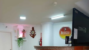 Uma área de recepção com balcão de madeira, um relógio, um extintor de incêndio e uma placa para Hostal Icetemario.