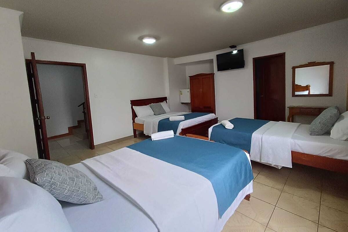 A hotel room with three beds, a television, a mirror, and a door leading to a hallway.