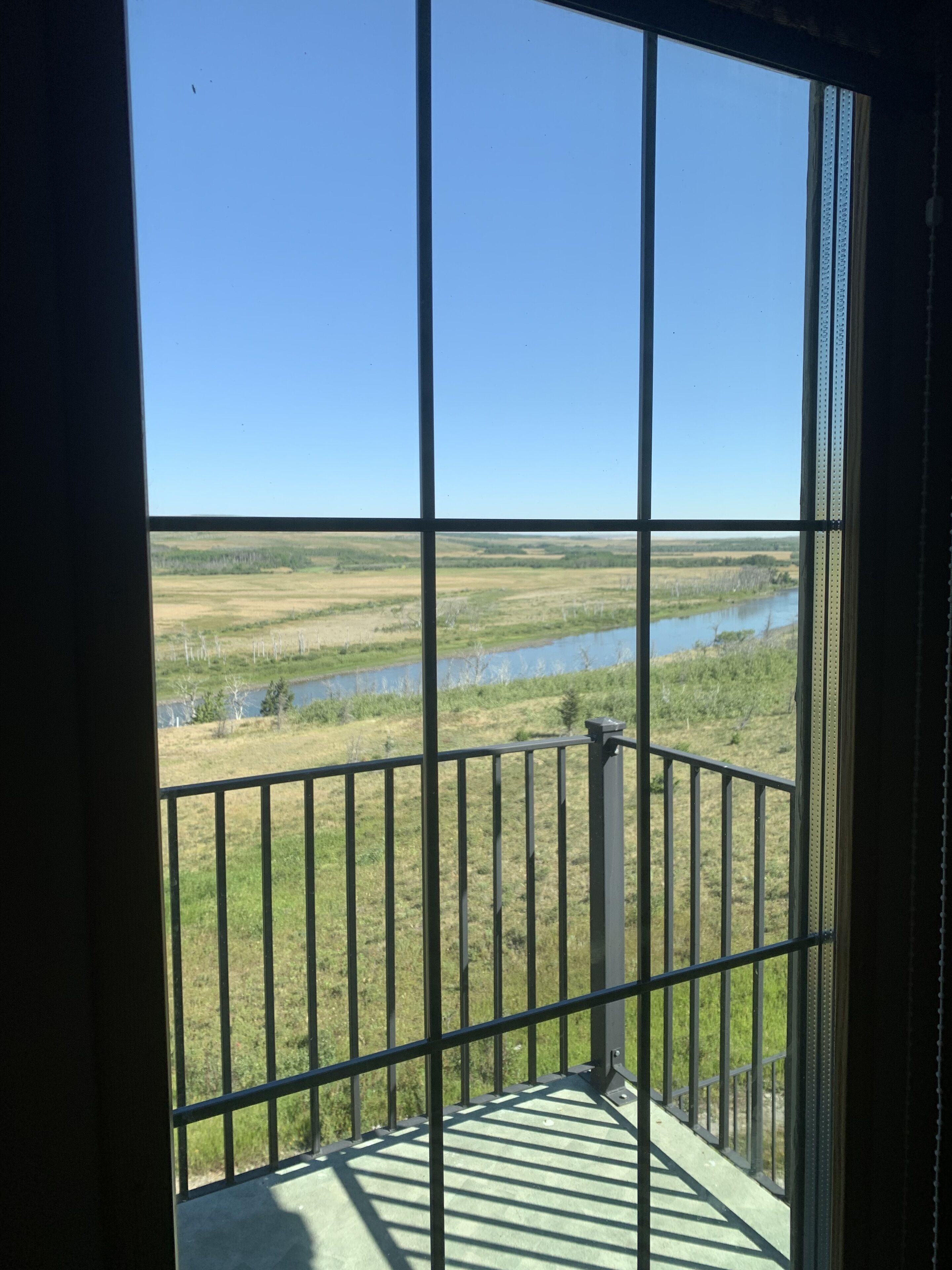 A balcony with a metal railing overlooking a grassy landscape and a body of water.