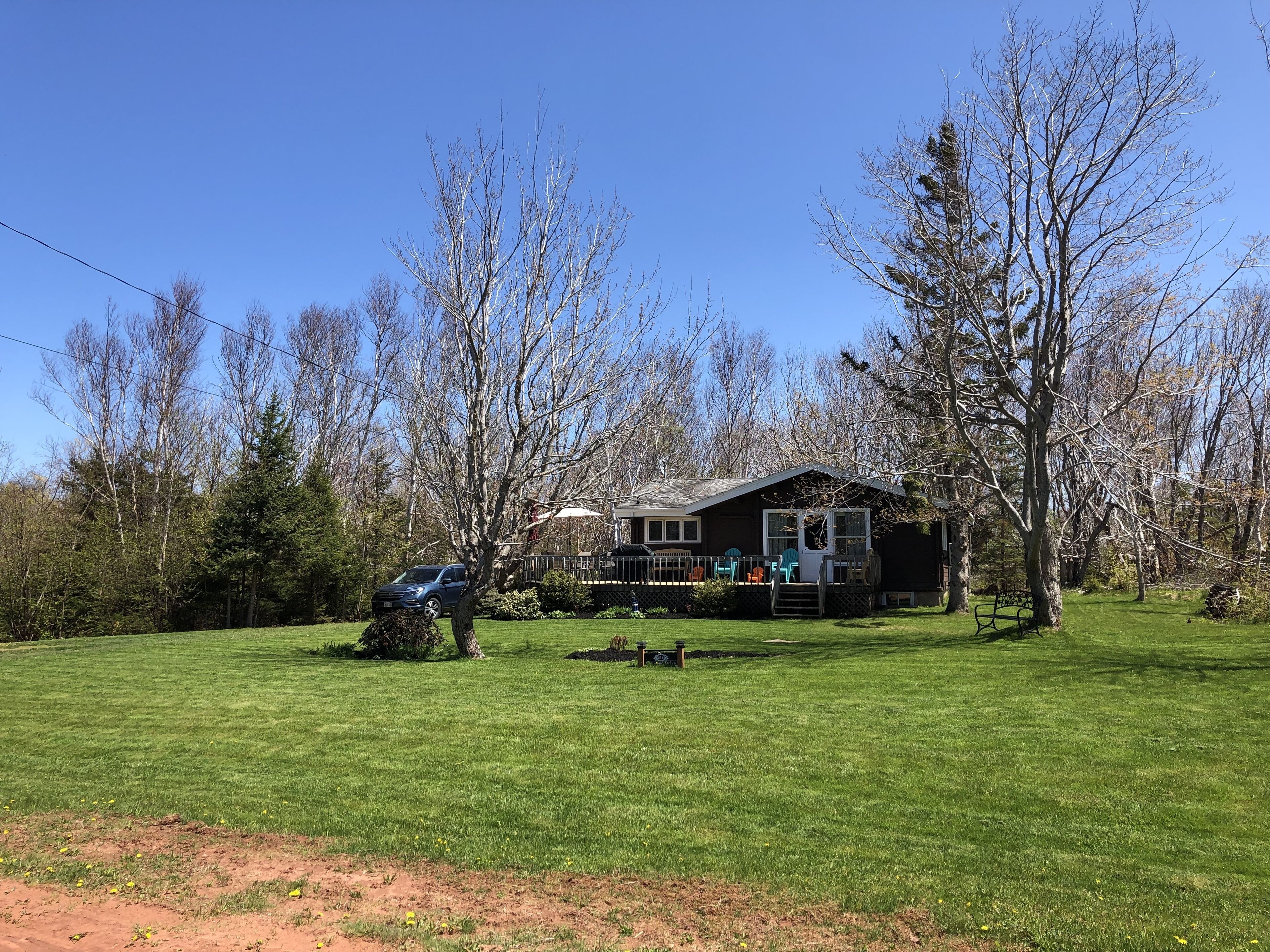 A house with a deck, surrounded by a grassy yard and trees.