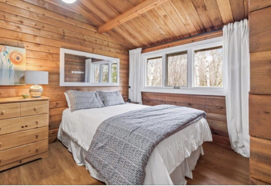 Une chambre dans une cabane en bois, avec un lit, une commode et une fenêtre avec des rideaux.