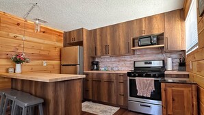A modern kitchen with wooden cabinetry, stainless steel appliances, and a bar area with stools. - Water Rafts + Trails - North Star by Janix Escapes. (Wellston)