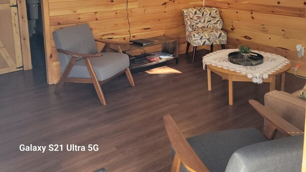 A cozy cabin interior with wooden walls, a flat-screen TV mounted on the wall, a small table with a plant, and two chairs. - Water Rafts + Trails - North Star by Janix Escapes. (Wellston)