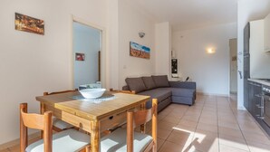 A dining area with a wooden table and chairs, a gray sofa, and a kitchen area with cabinets. - GuestHost - Porta Maggiore Apartment (Bologna)