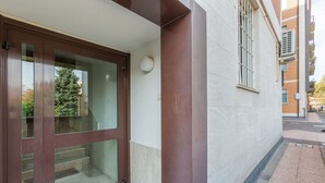 A building entrance with a glass door, a brown column, and a window with bars. - GuestHost - Porta Maggiore Apartment (Bologna)