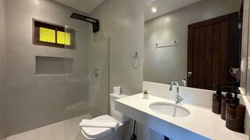 Un baño moderno con cabina de ducha de vidrio, inodoro blanco, un espejo grande y lavabo blanco con dispensadores de jabón.