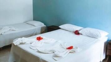 Quarto de hotel com duas camas de solteiro e uma cama de casal, tudo arrumado com lençóis brancos e flores vermelhas.