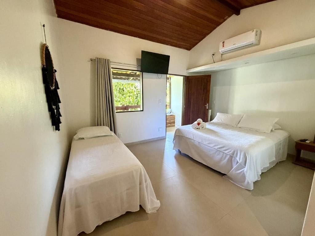 Une chambre avec deux lits simples, un téléviseur fixé au mur, un appareil de climatisation et une fenêtre avec des rideaux.