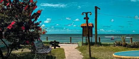 A pathway leading to a beach with a bench and a table, surrounded by greenery and a view of the ocean.