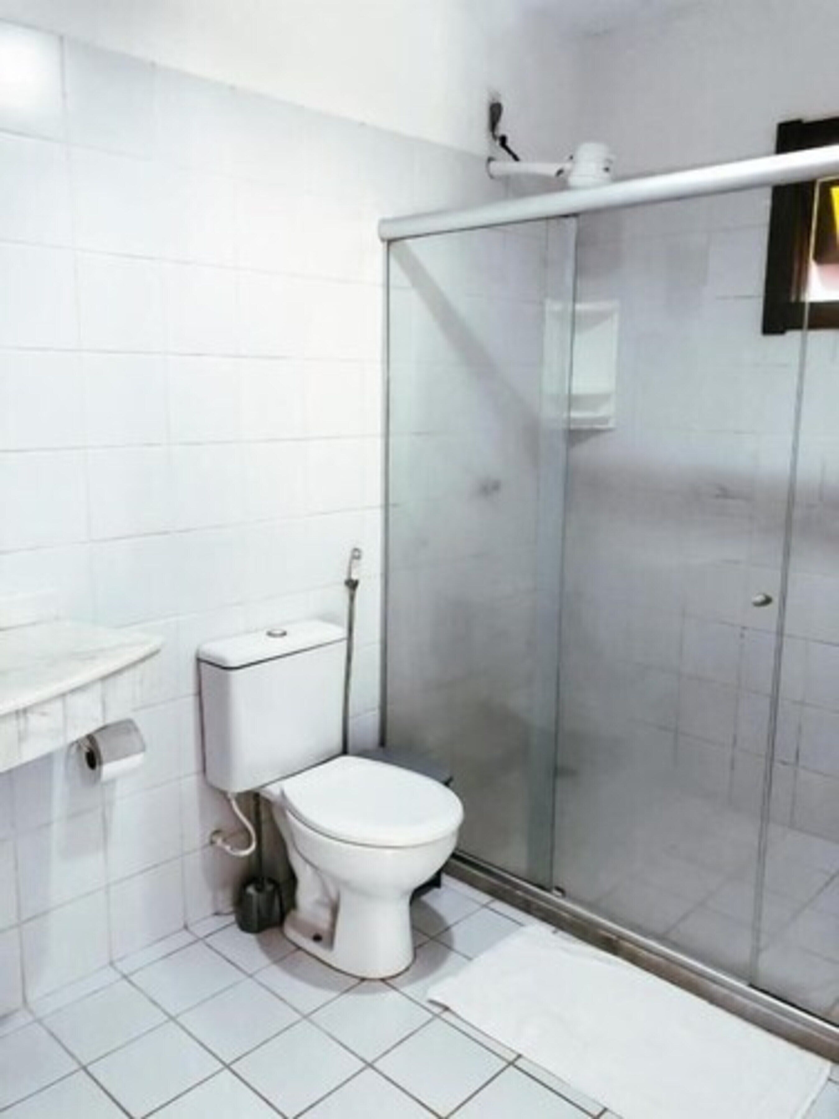 A bathroom with a toilet, a glass shower enclosure, and a white tiled floor.