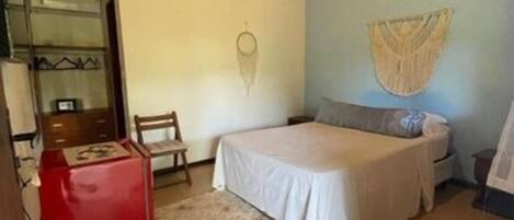 A bedroom with a bed, a chair, a small table, and a wall hanging.