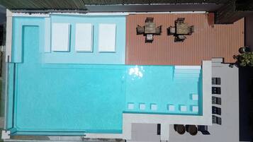 Un área de piscina en la azotea con piscina azul, terraza de madera y mesa con sillas.