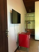 Quarto com televisão na parede, um armário vermelho e uma porta com fechadura.