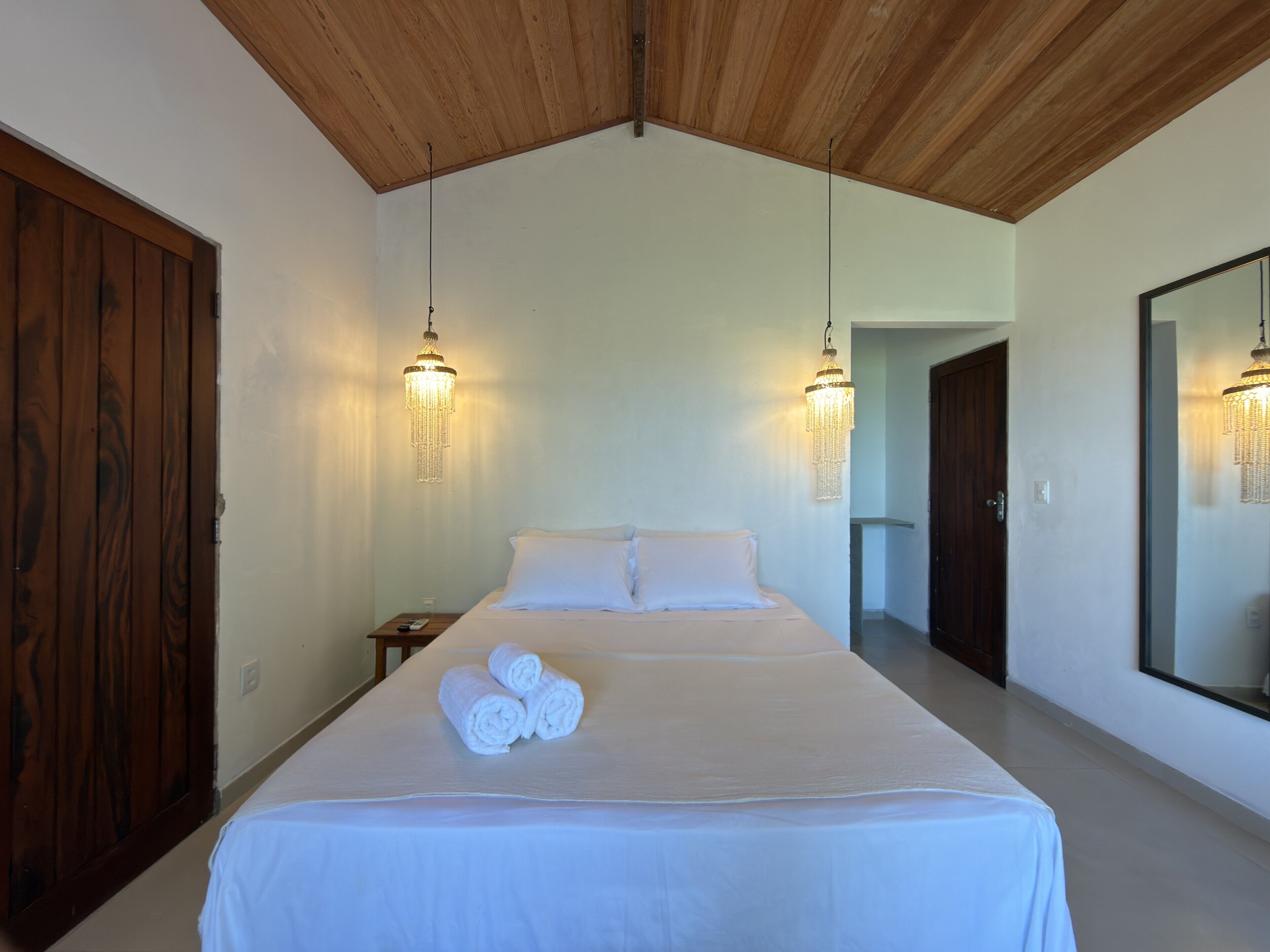 Un dormitorio con una cama grande, techo de madera, dos candelabros en la pared y un espejo amplio.