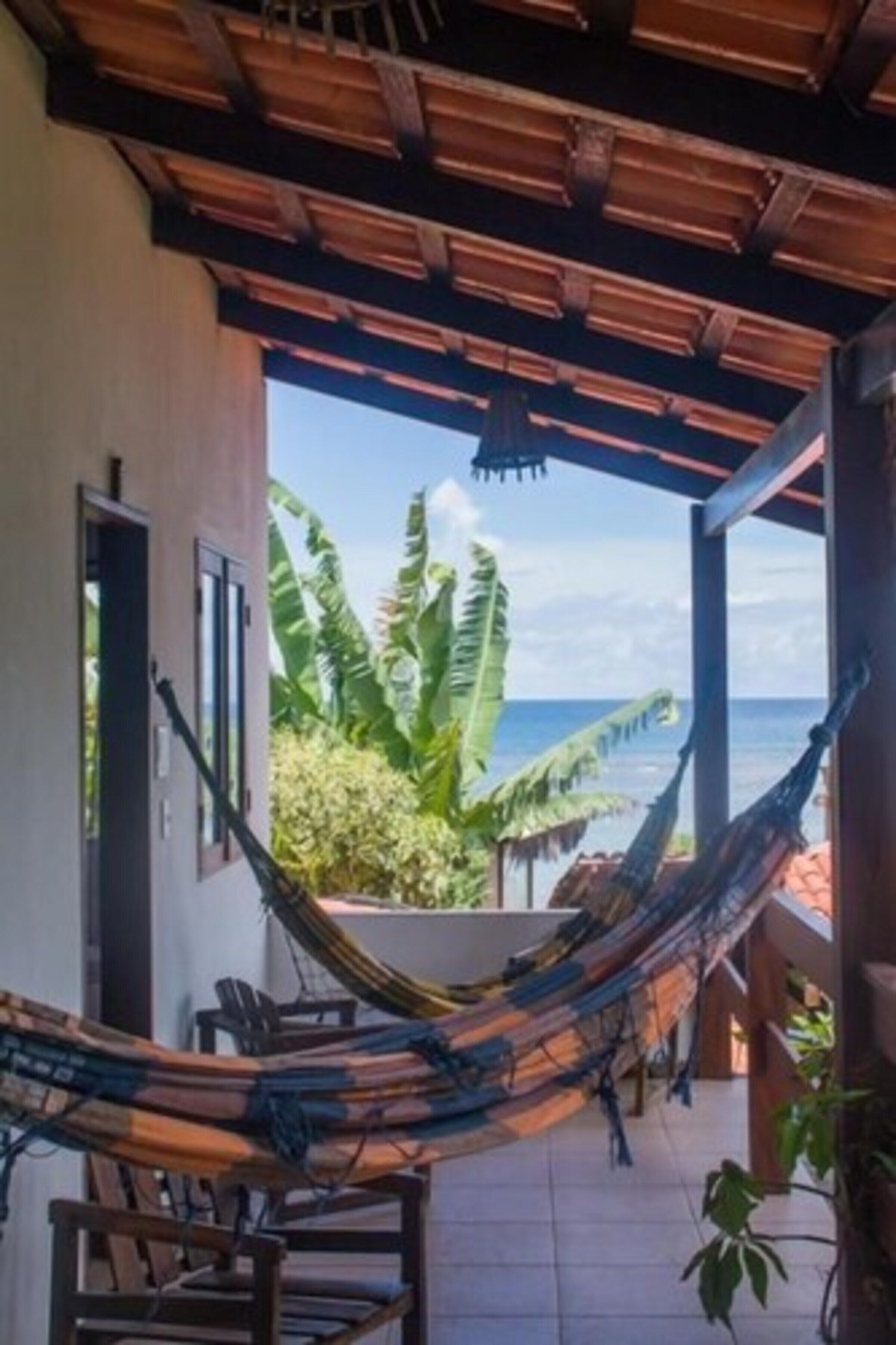 Uma rede sob uma pérgola de madeira com vista para o oceano e plantas tropicais.