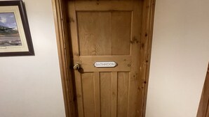 Eine Holztür mit einem Schild, auf dem "BADEZIMMER" steht, und einem gerahmten Bild links an der Wand.
