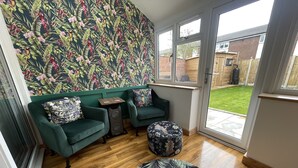 Ein Zimmer mit zwei grünen Sofas, einem runden Hocker, einem kleinen Tisch und einer Wand mit floralem Muster.