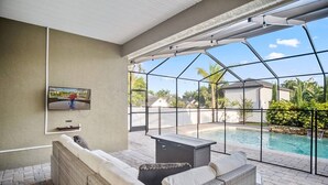 Un patio techado con piscina, mobiliario exterior y televisor.