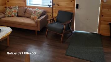 Ein gemütliches Zimmer mit Holzvertäfelung, einer Couch mit floralen Kissen, einem Sessel, einer Lampe und einem Schild mit der Aufschrift 'hello'.