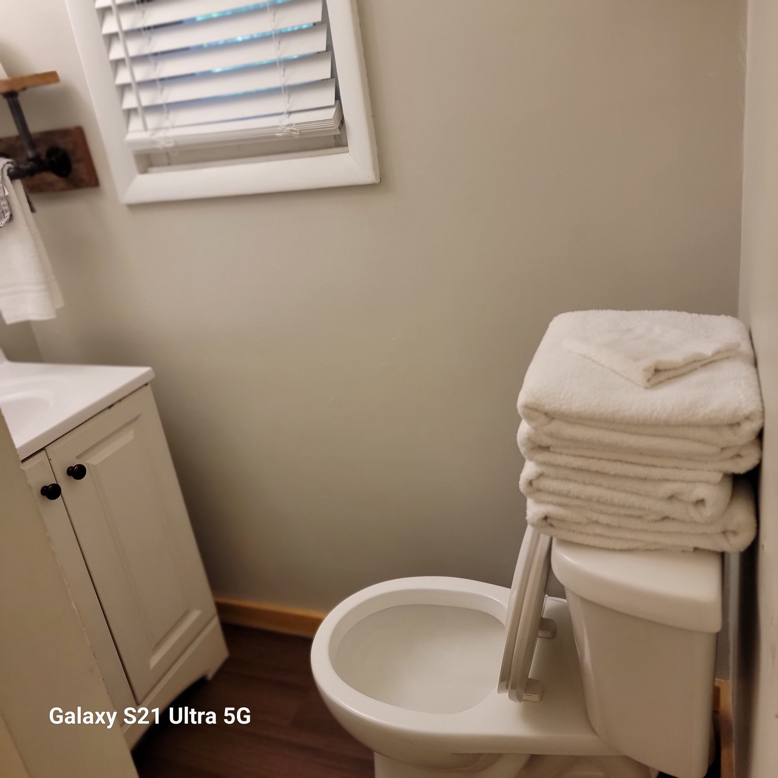 Une salle de bain avec des toilettes, un lavabo et une fenêtre avec des stores.