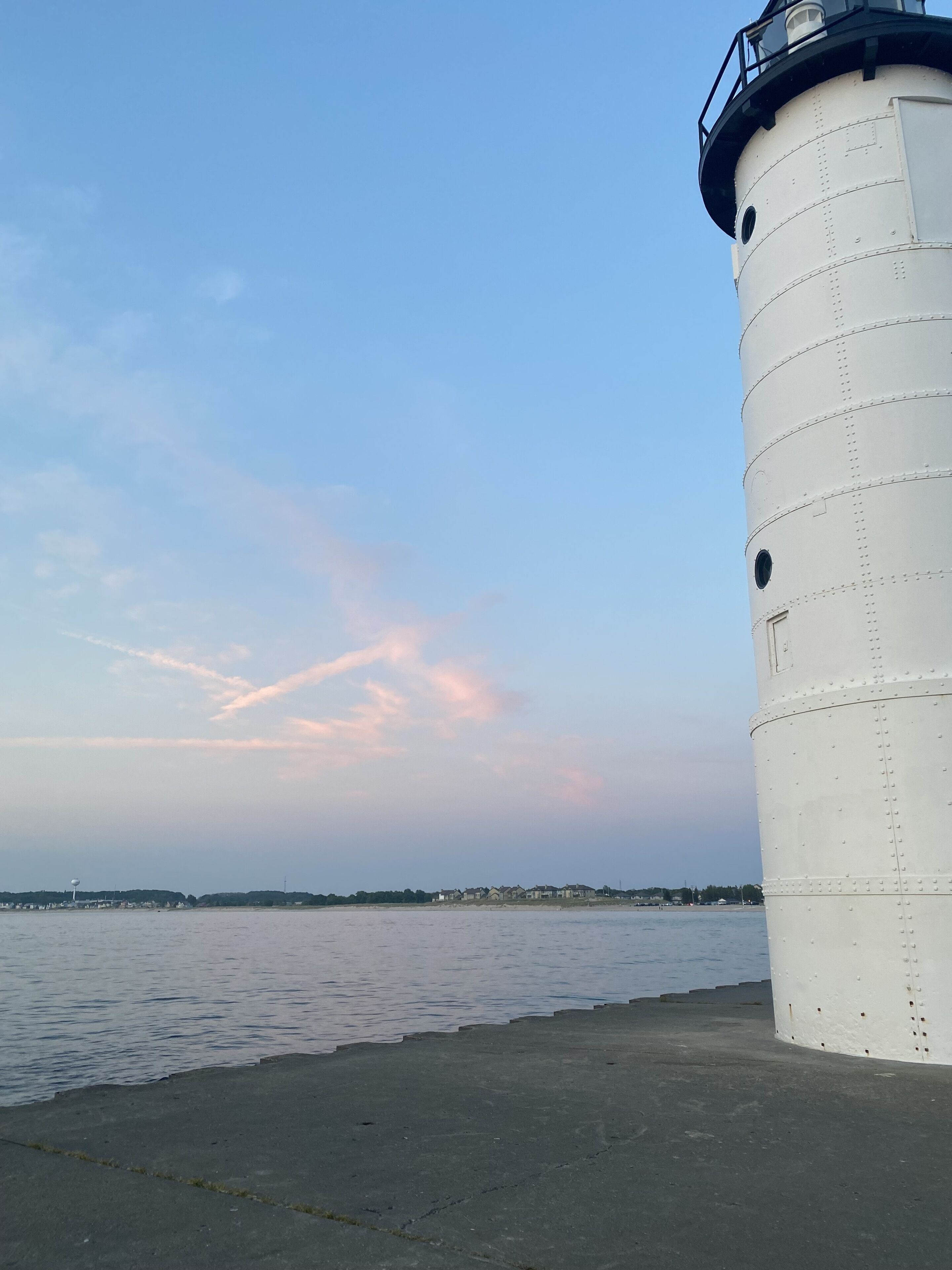 A white cylindrical structure, likely a lighthouse, by a calm body of water with a distant shoreline.