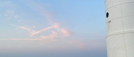 A white cylindrical structure, likely a lighthouse, by a calm body of water with a distant shoreline.