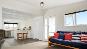 A modern living room with a sofa, a kitchen area, and a dining space. - LAKE VIEW RETREAT - Relax, Unwind, & Make Memories (Mangakino)