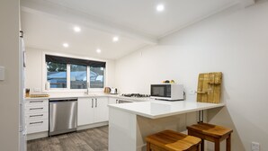 A modern kitchen with white cabinetry, a stainless steel dishwasher, a microwave, and a wooden island with two stools. - LAKE VIEW RETREAT - Relax, Unwind, & Make Memories (Mangakino)