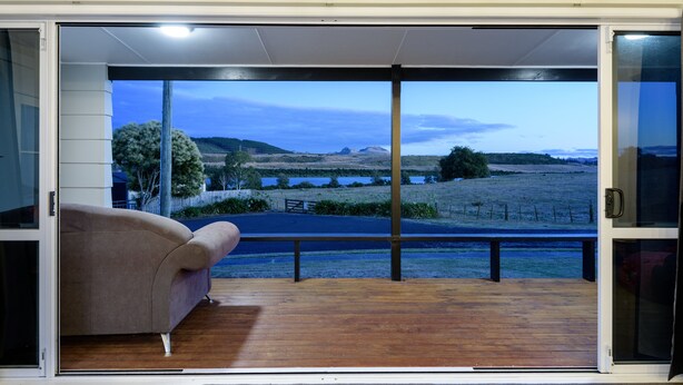 A room with a sliding glass door leading to a deck with a view of a landscape. - LAKE VIEW RETREAT - Relax, Unwind, & Make Memories (Mangakino)