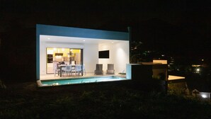 A modern house with a pool, a dining area, and a kitchen visible through the glass doors. - Residence BO, One-Bedroom Apartment, Suite with Sea View (Baie Orientale)
