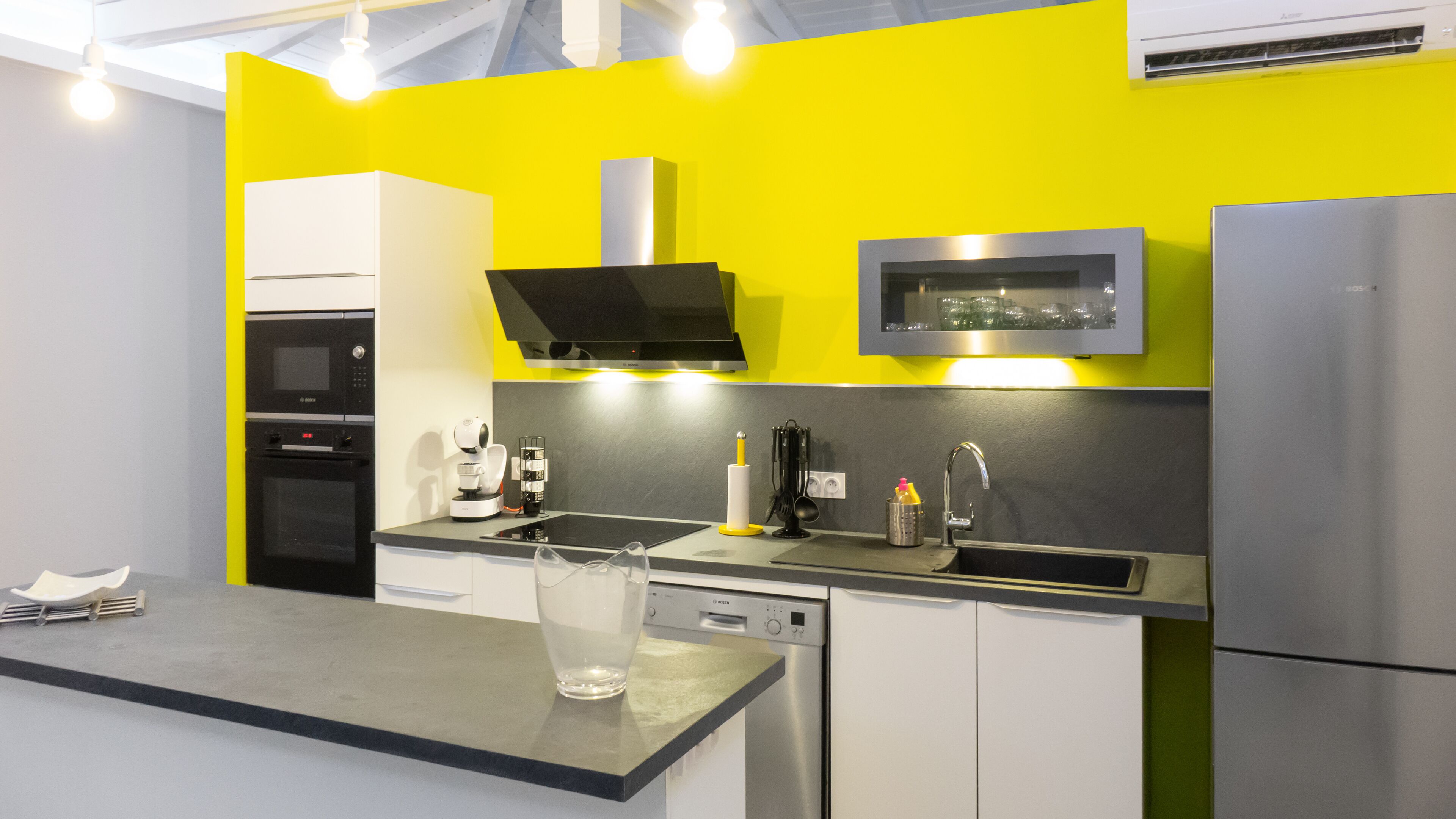 Une cuisine moderne avec un mur jaune vif, des appareils en acier inoxydable et un plan de travail noir.