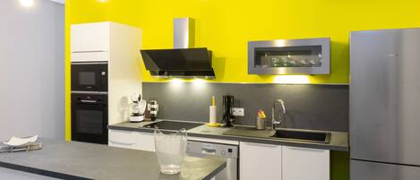 Une cuisine moderne avec un mur jaune vif, des appareils en acier inoxydable et un plan de travail noir.
