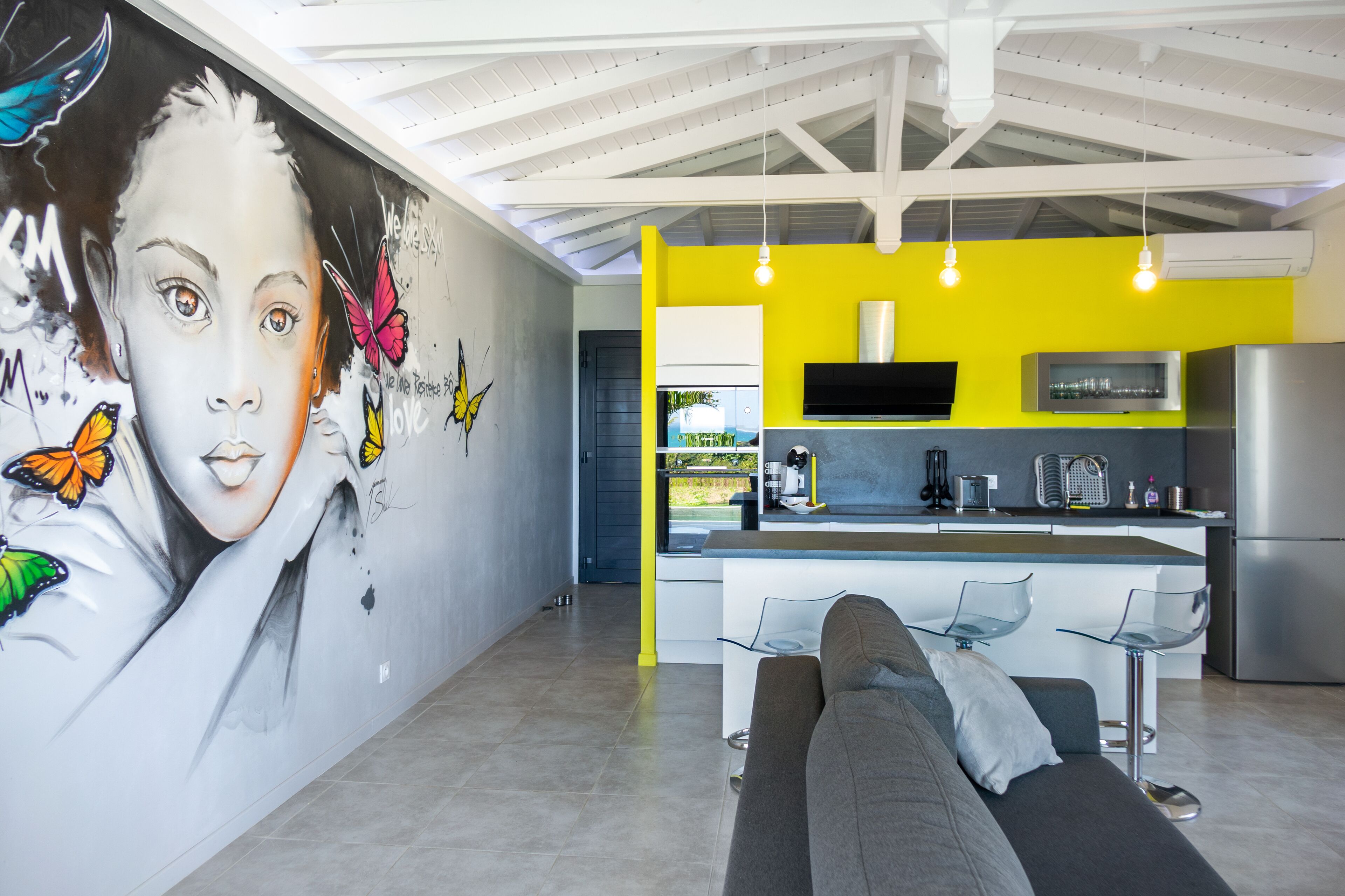 A modern kitchen with a yellow accent wall, a built-in oven, and a stainless steel refrigerator.