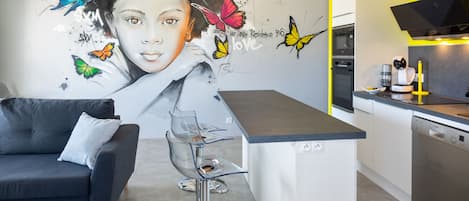 A modern kitchen with a grey sofa, a bar stool, and a mural with butterflies and text.