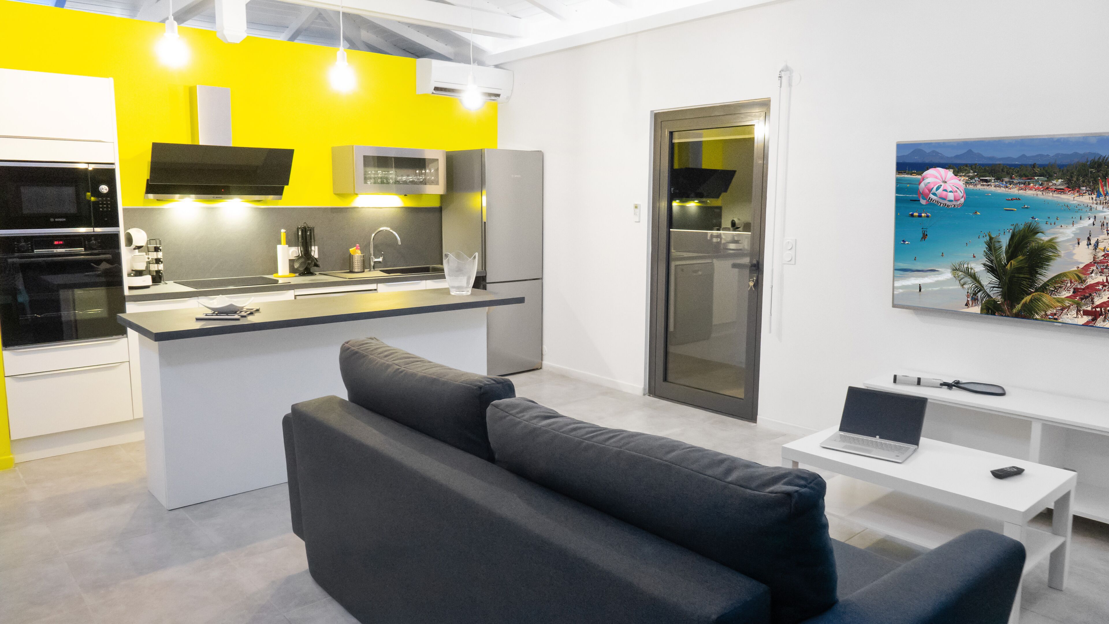 Una cocina moderna con una isla central, un área de comedor con un sofá y un portátil sobre una mesita.