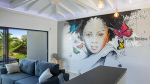 A modern living room with a large mural, a sofa, and a dining area. - Residence BO, One-Bedroom Apartment, Suite with Sea View (Baie Orientale)