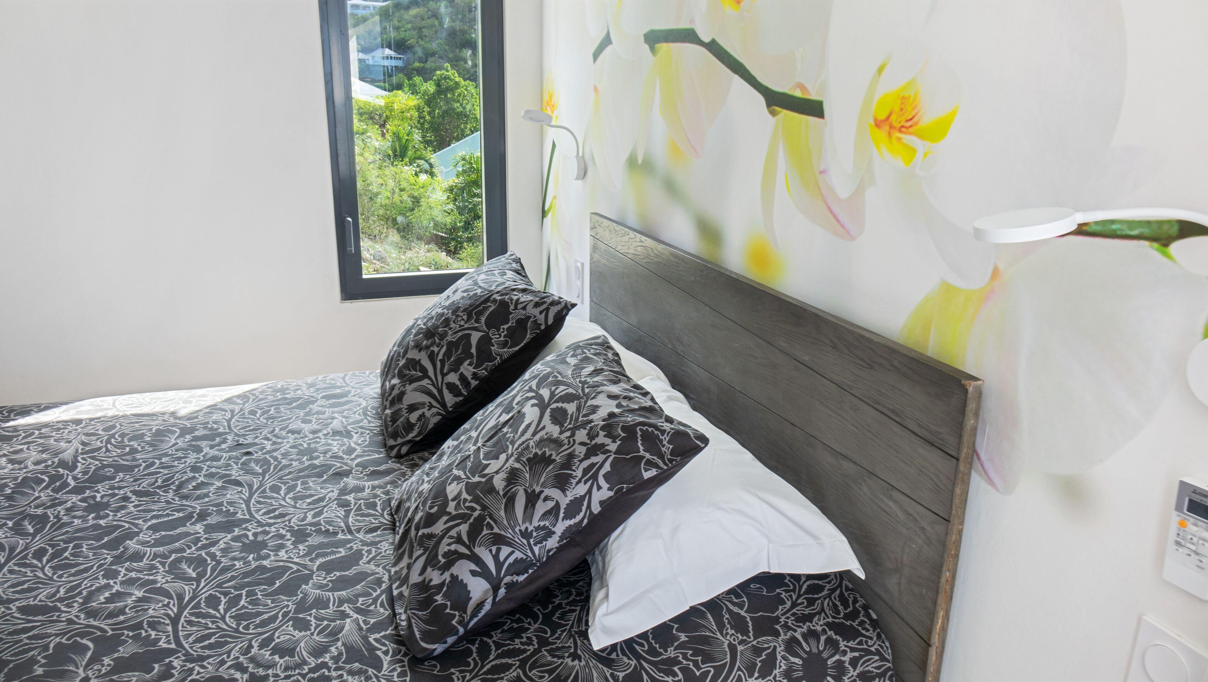 Une chambre à coucher avec un lit, un papier peint à motifs floraux et une fenêtre donnant sur un paysage verdoyant.