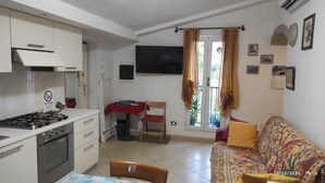 A compact kitchen with a gas stove, a dining table with chairs, a sofa, and a TV mounted on the wall. - 2.5 km from the sea of Levanto, on the first hill, in a green and quiet location (levanto)