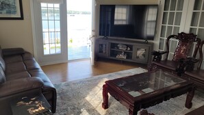 A living room with a brown leather sofa, a glass coffee table, and a TV on a stand. - Pinnacle of St. Andrews by the Sea - Exquisite seaside home. (St. Andrews)