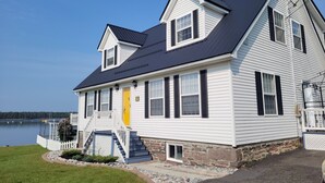 A two-story house with a dark roof, white siding, and black shutters. It has a front porch with steps and a yellow door. - Pinnacle of St. Andrews by the Sea - Exquisite seaside home. (St. Andrews)